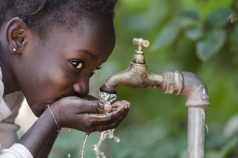 african american child drinking water from a faucet with her hands